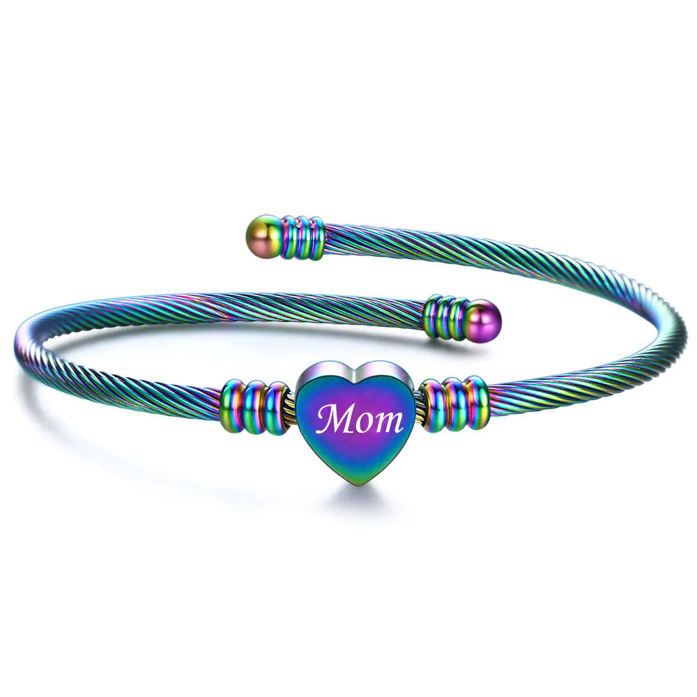 A stainless steel braided bracelet with a heart-shaped charm that has the word 'Mom' on it, displayed against a white background.