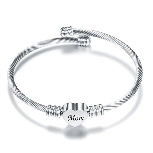 A stainless steel braided bracelet with a heart-shaped charm that has the word 'Mom' on it, displayed against a white background.