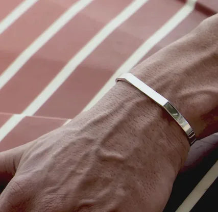 A stainless steel bracelet with a sleek, flat design, worn on a person's wrist.