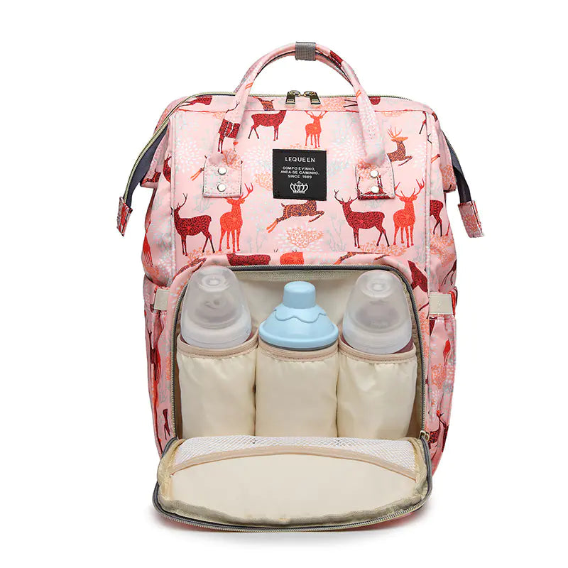 A pink mommy bag with a deer print, featuring multiple compartments including two baby bottles and a diaper, with a shoulder strap and a top handle.
