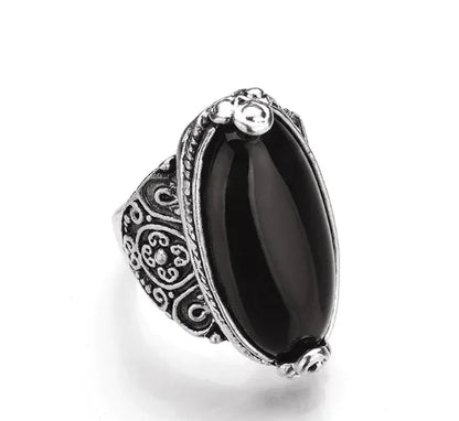 A ring with a large black stone set in a silver-colored mounting with intricate designs around the band.