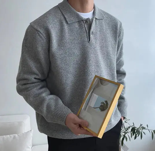 A man sitting at a table wearing a black long-sleeved polo collar buttoned sweater, with a white cup on the table.
