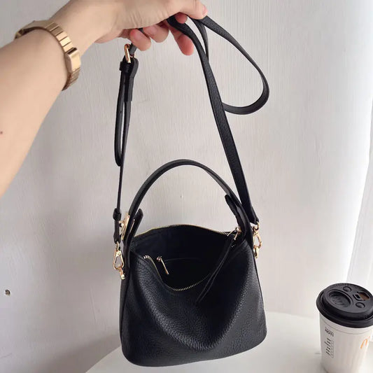 A black cowhide leather lunch box bag with a shoulder strap, displayed in hand against a neutral background.