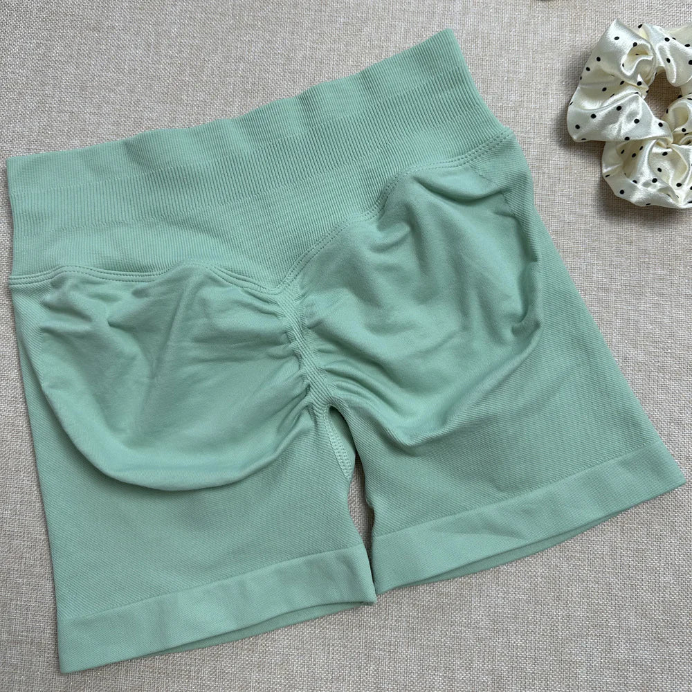 A pair of blue yoga shorts laid flat on a surface, with a high-waist fit and a small amount of stretch fabric visible.
