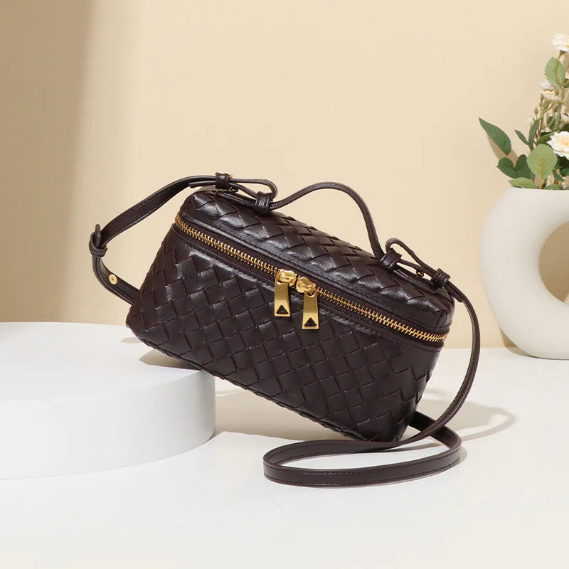 A brown woven shoulder bag with a quilted design, featuring a zippered top, a detachable strap, and placed on a white surface.